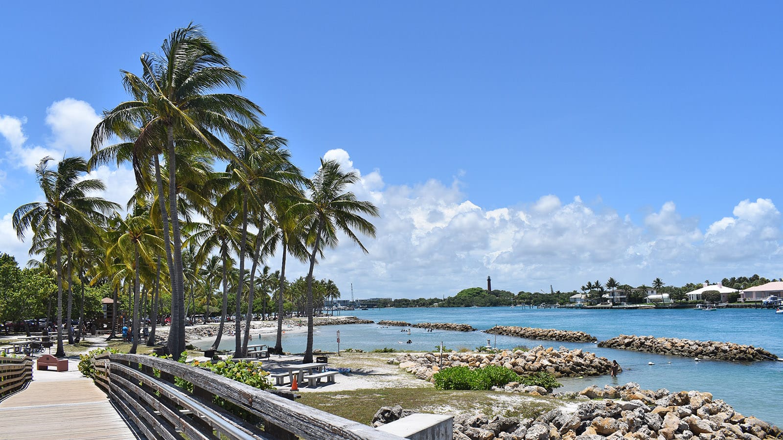 Blue water inlet with breakwaters, homes, a park, and a lighthouse in the distance