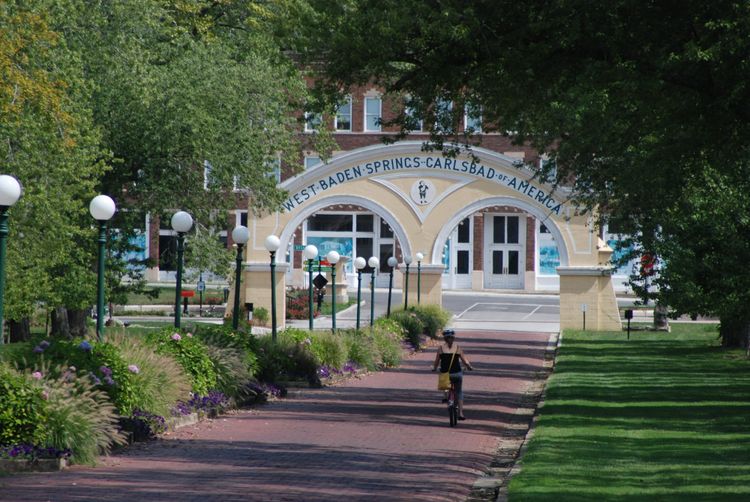 Woman on bicycle heading down brick road towards classical archway