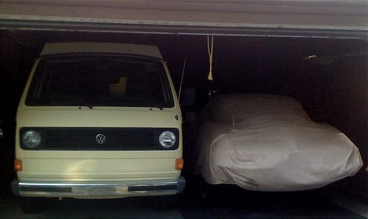 A VW Westfalia looms next to shorter vehicles in a dark garage