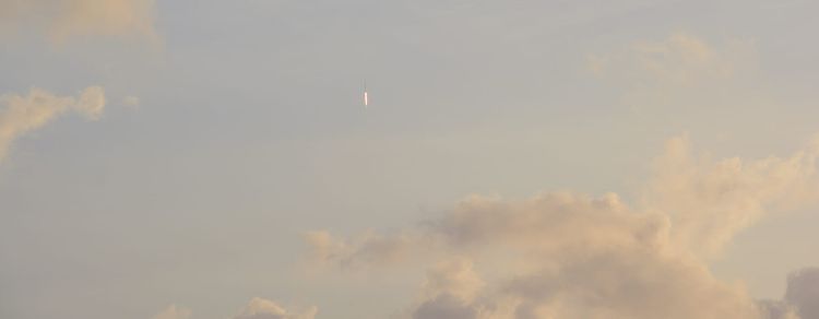 Rocket with streak of flame pointed straight up into a cloudy sky