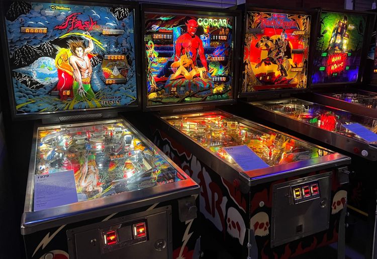 A set of four pinball machines glowing in a darkened room
