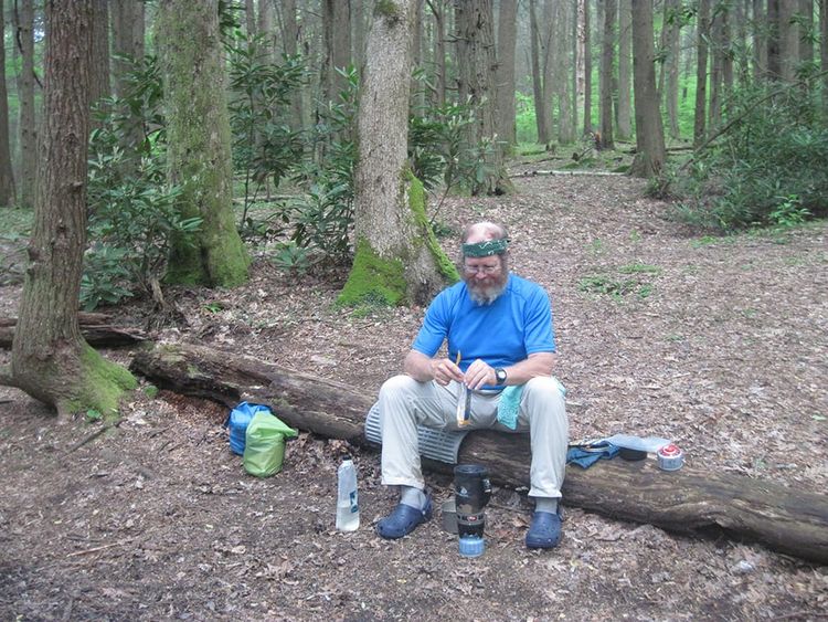 Man sitting on log making dinner on a camp stove