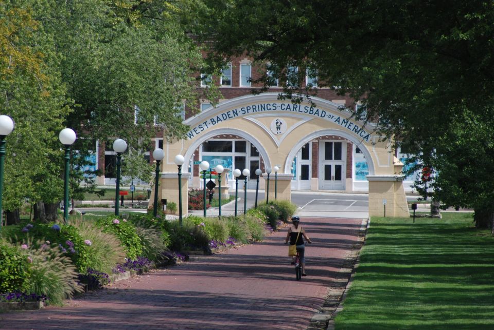 Woman on bicycle heading down brick road towards classical archway