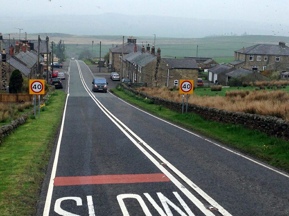Two lane road through a small rural English village with stone houses