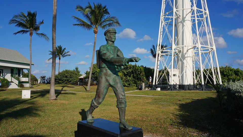 Statue of mailman in old time clothing near base of lighthouse