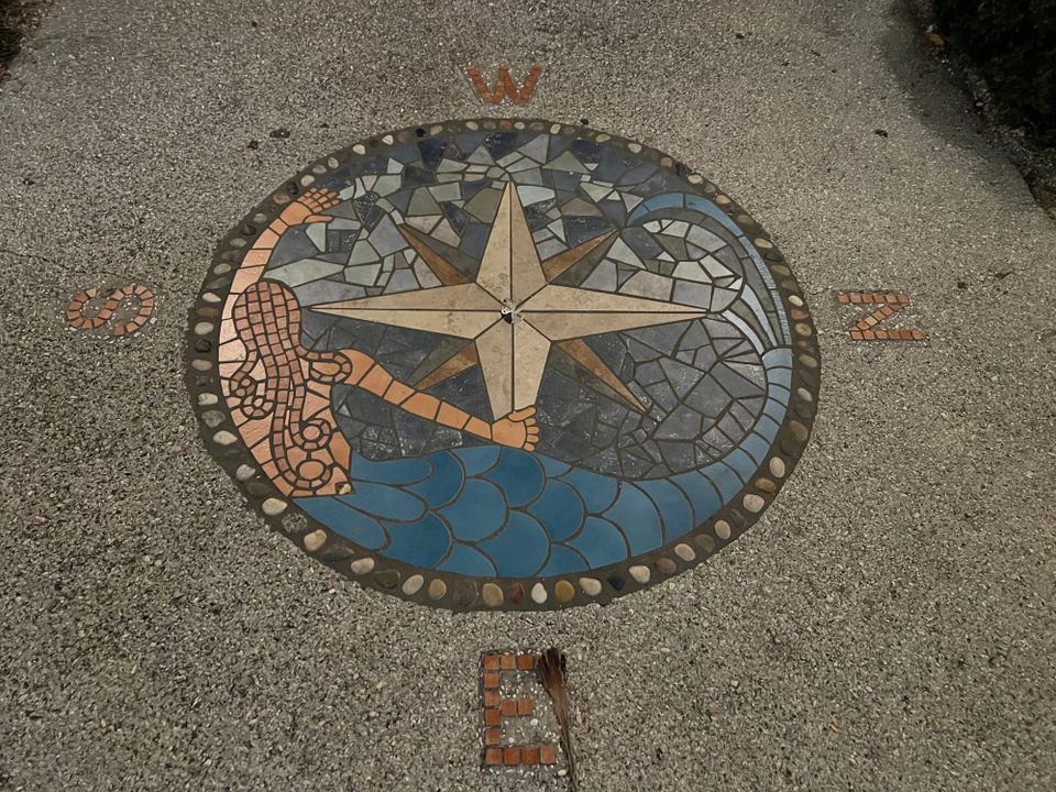 Mosaic tile compass set into sidewalk with artwork featuring a mermaid with hair like an octopus