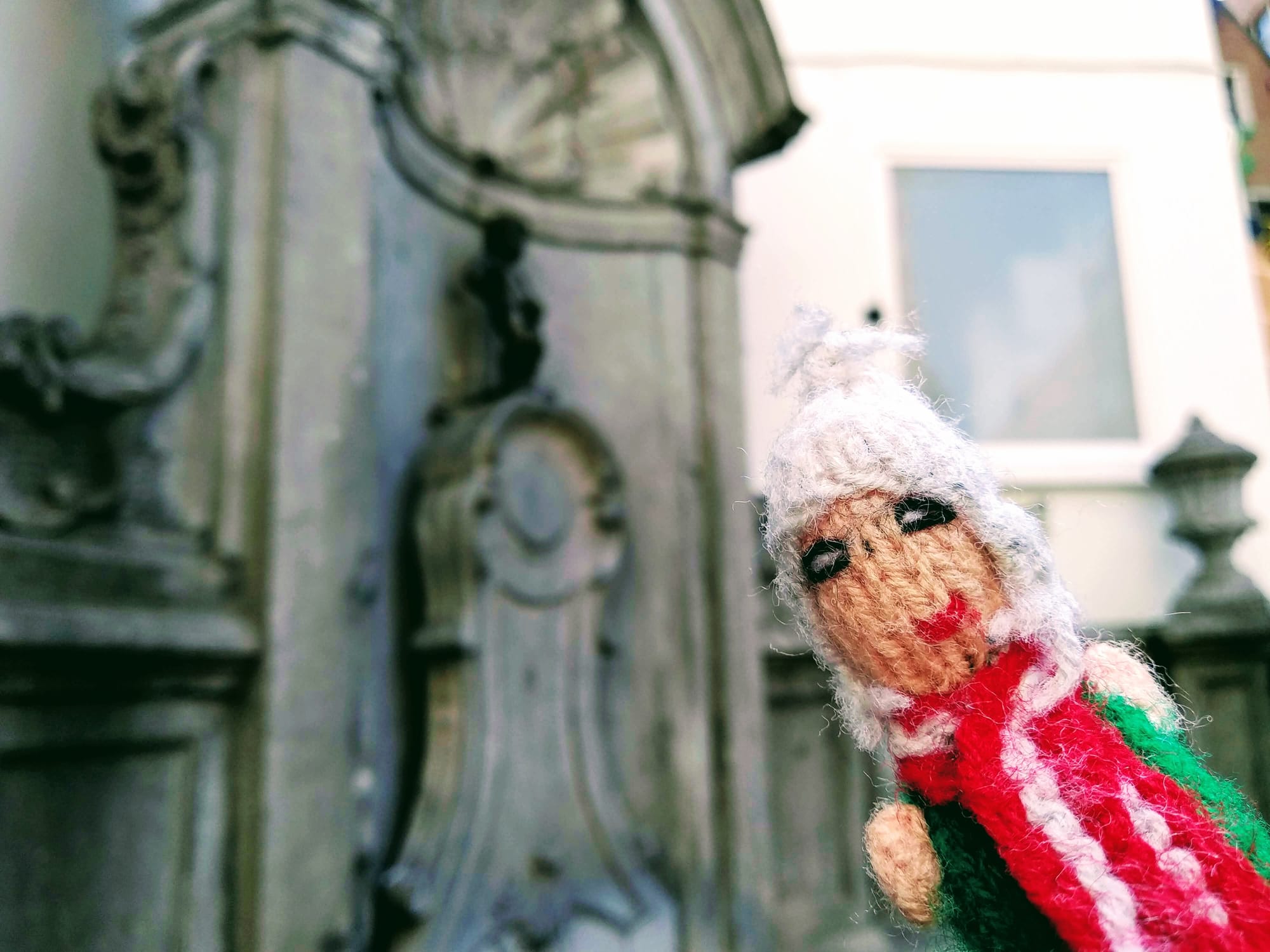 A hardened tourist in finger puppet form stands in front of the Manneken Pis statue in Brussels.