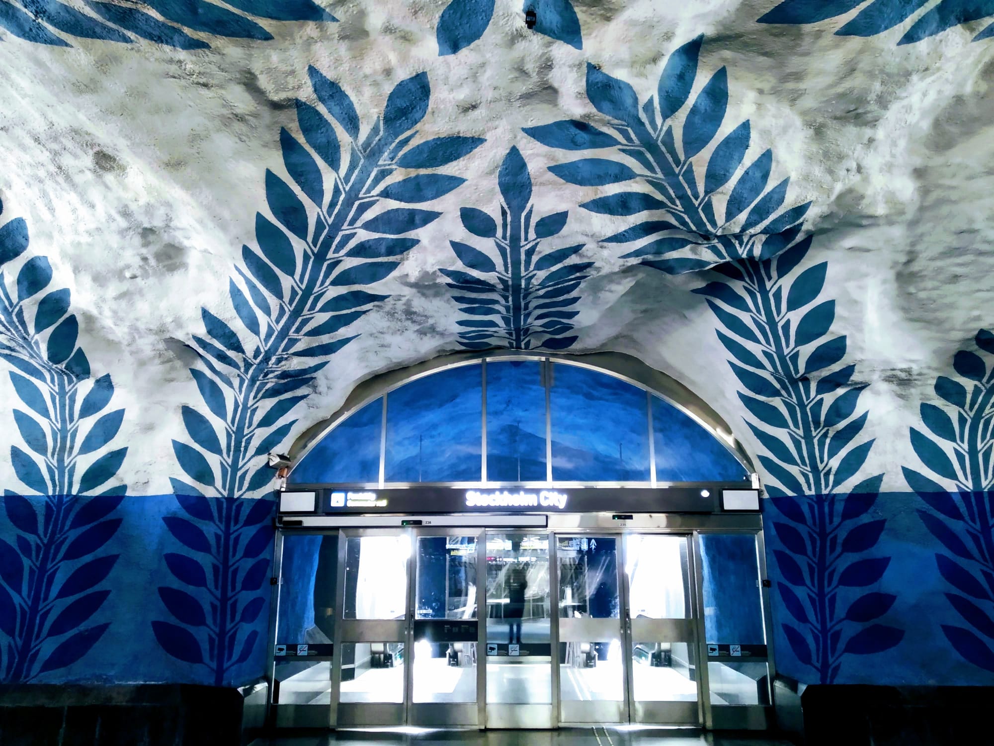 Blue leaf creepers decorate the white walls surrounding an entrance to Stockholm City.