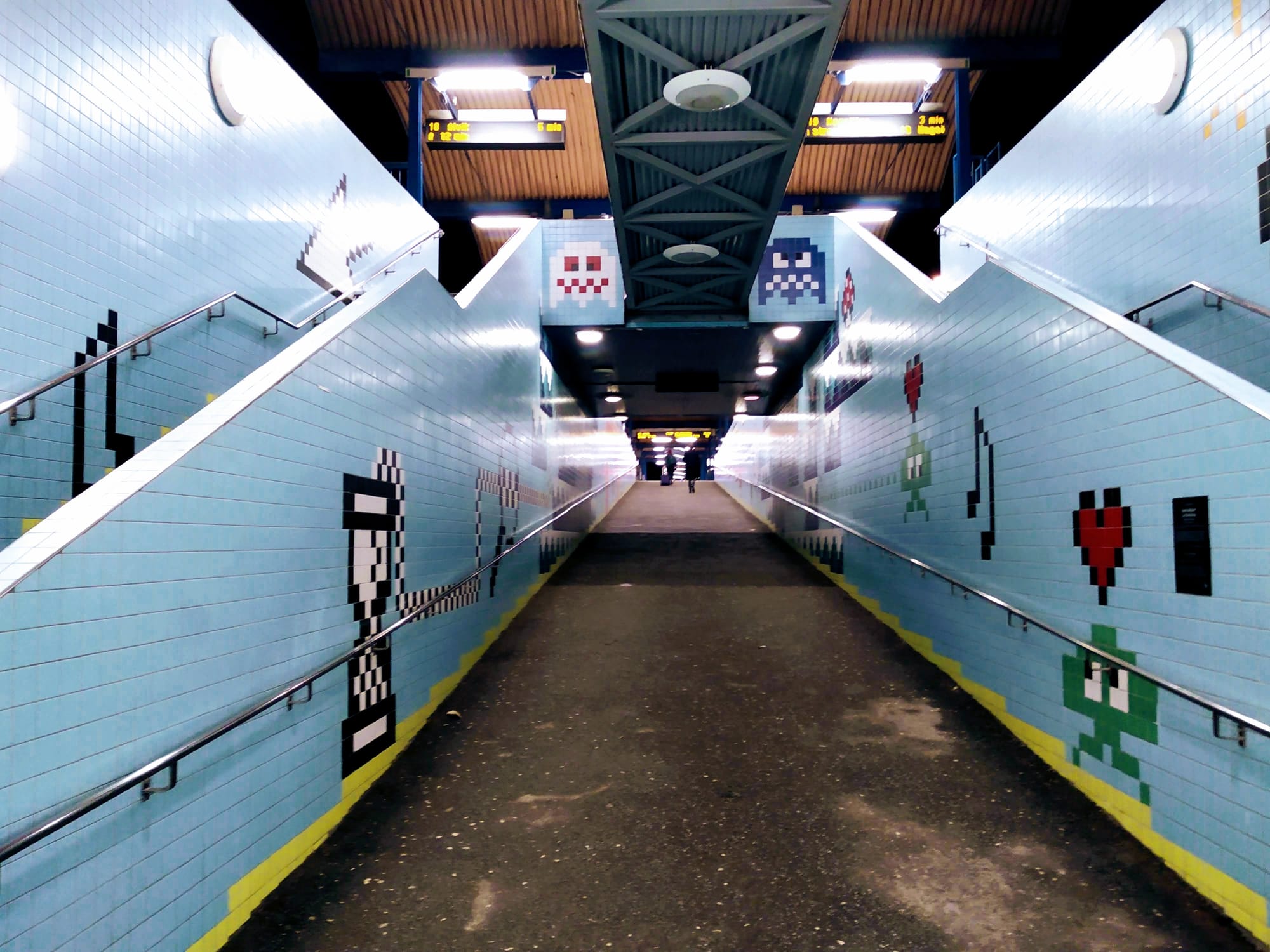 Pac-Man ghosts and other 8-bit characters adorn the blue tiled walls of a Stockholm metro station.