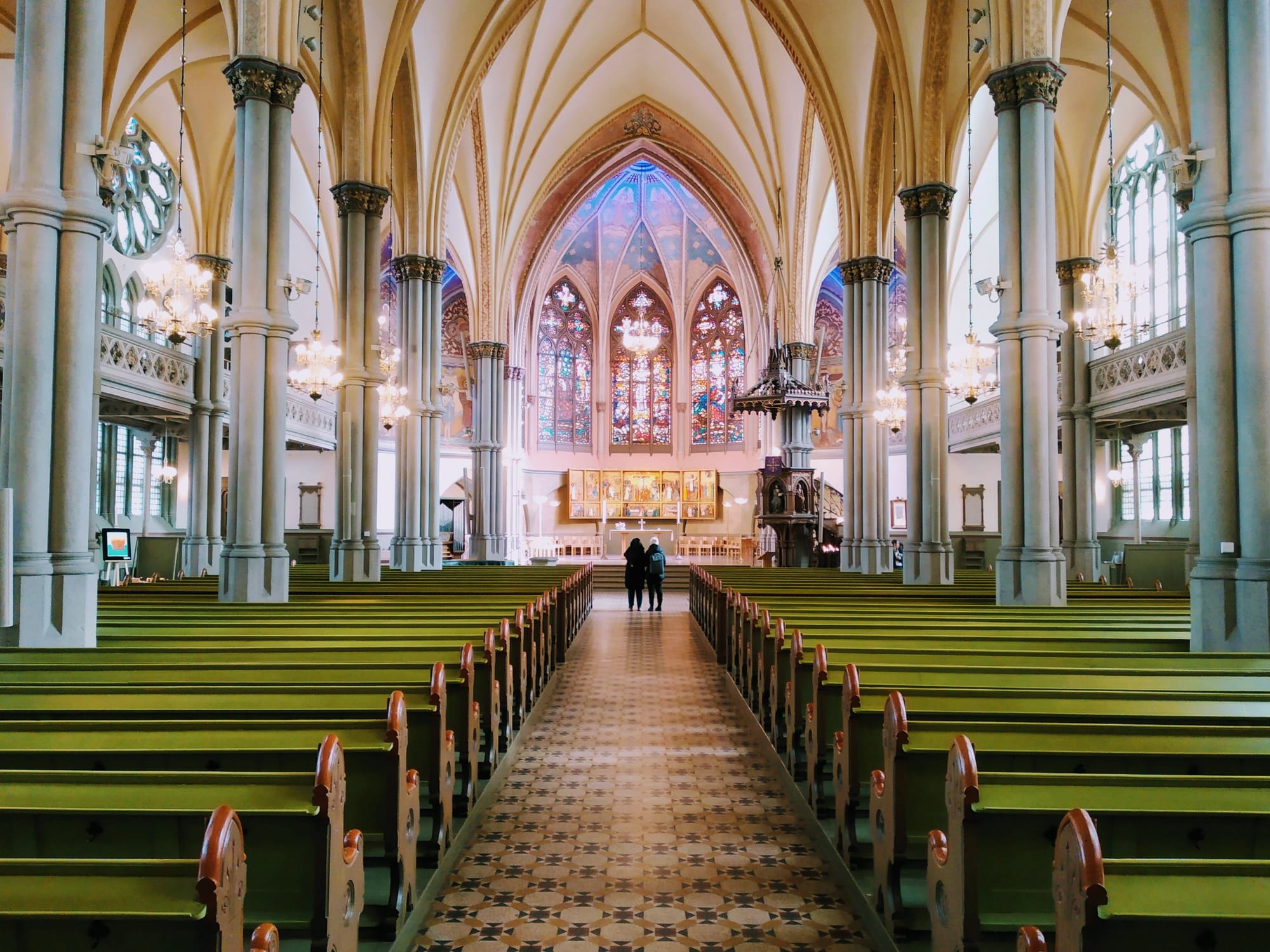 Two people pause in front of the colourful chancel of Oscar Fredriks Kyrka.