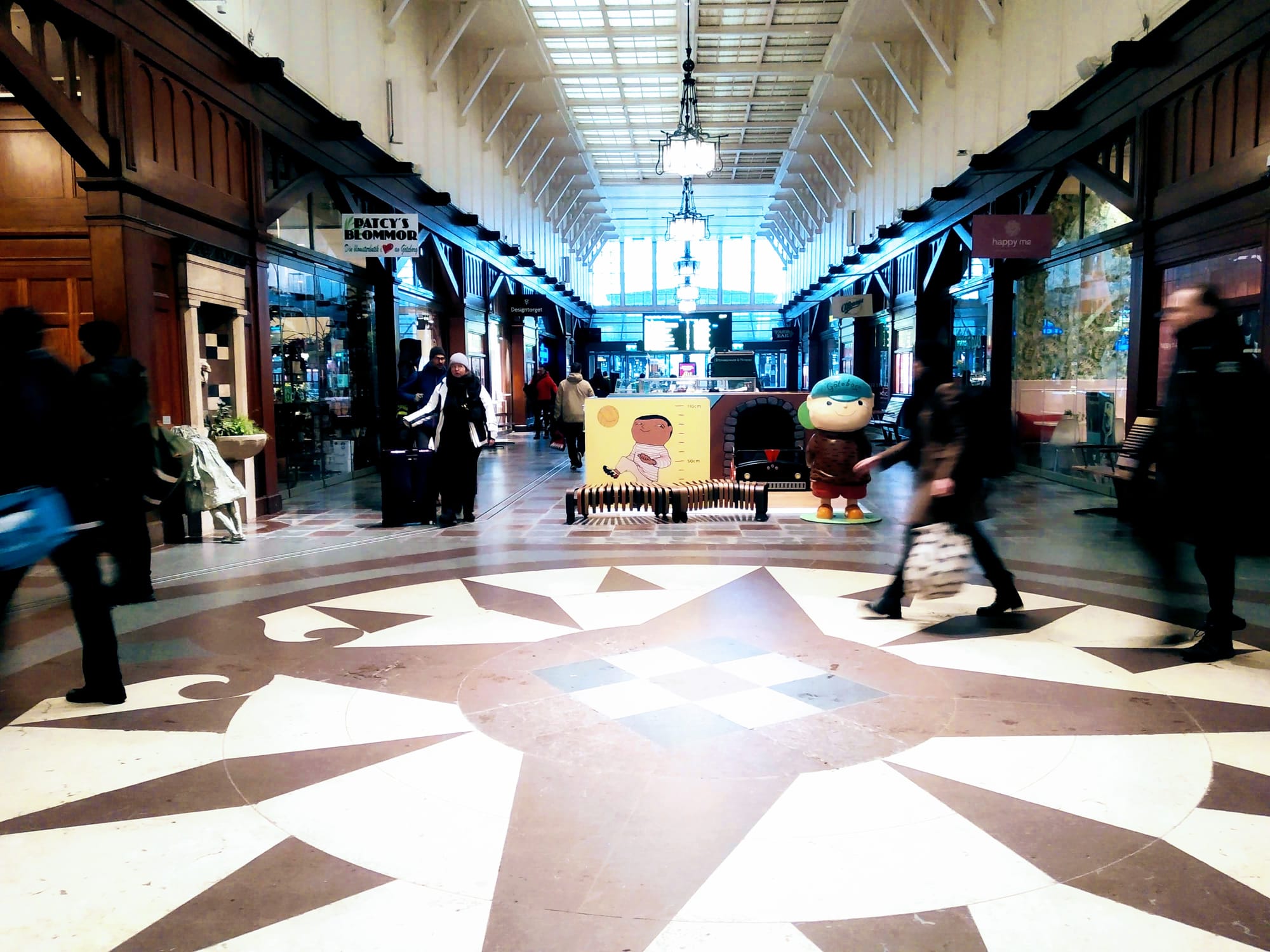 People walk through Gothenburg central station past the children's play area and the statue of the Weeping Girl.