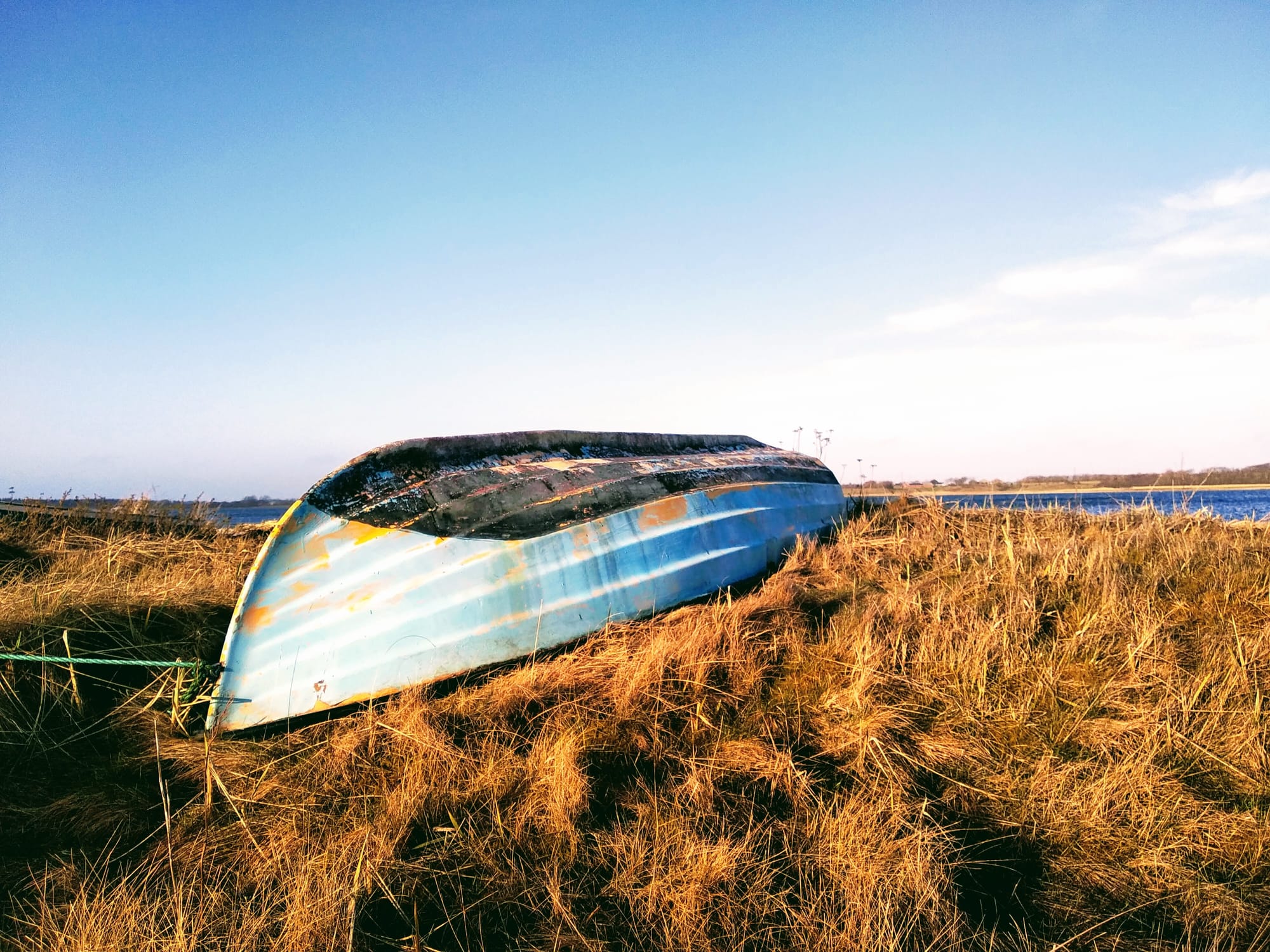An upturned light-blue boat on yellow grass at the edge of a fjord.