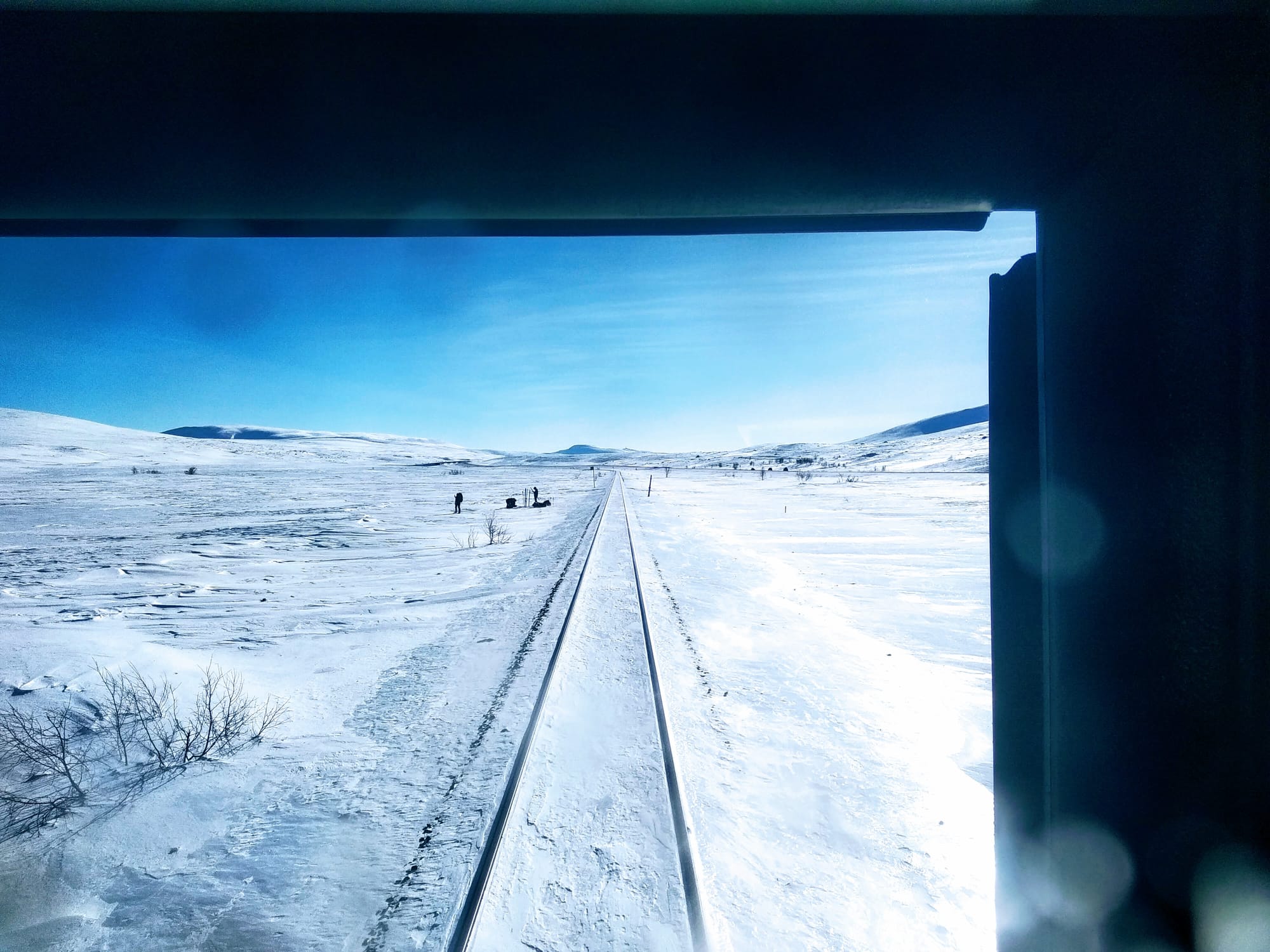People walk through the snow along a single railway line stretching to the horizon.