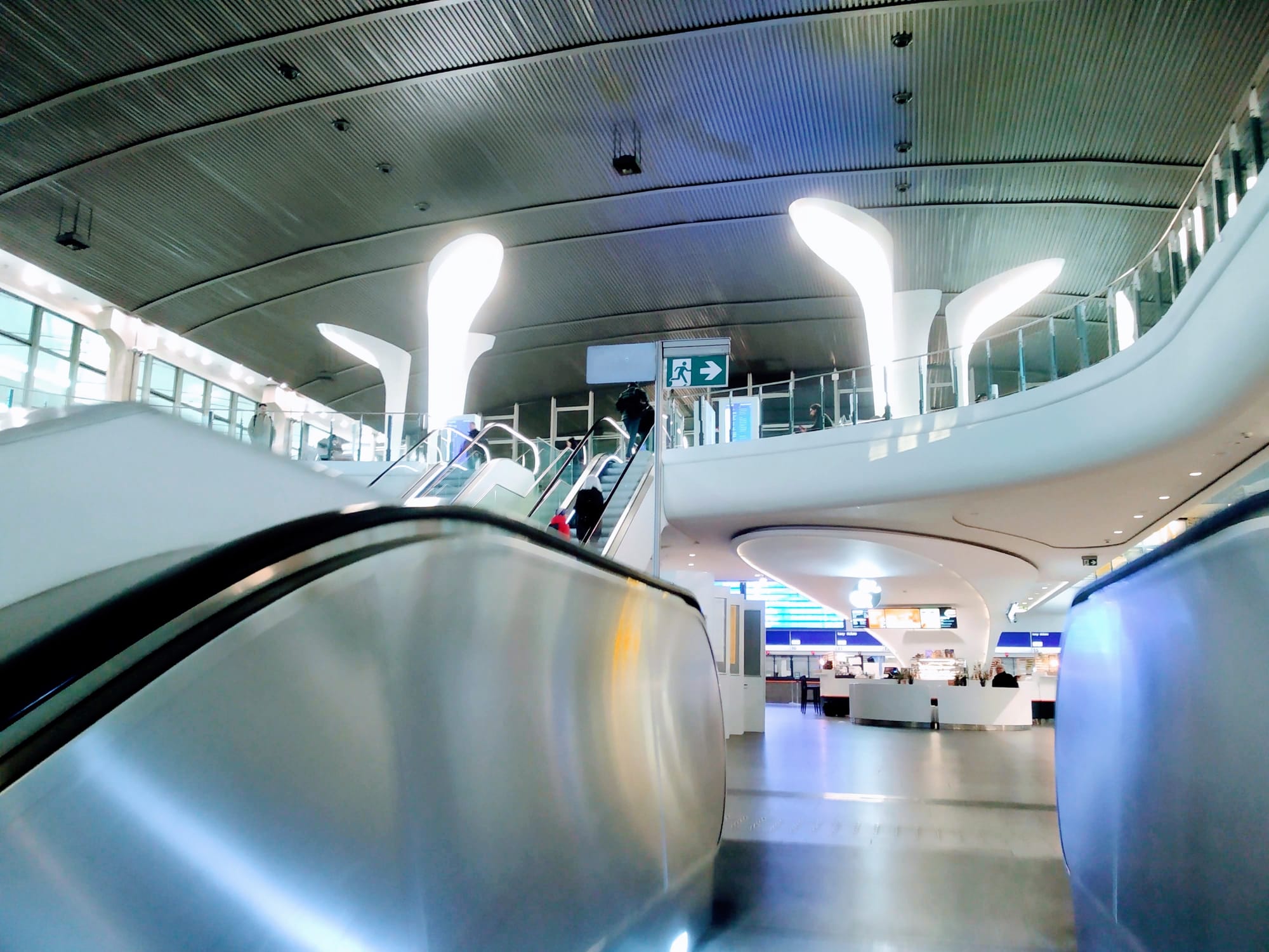 People ride an escalator in a bright-lit Warsaw Central station.