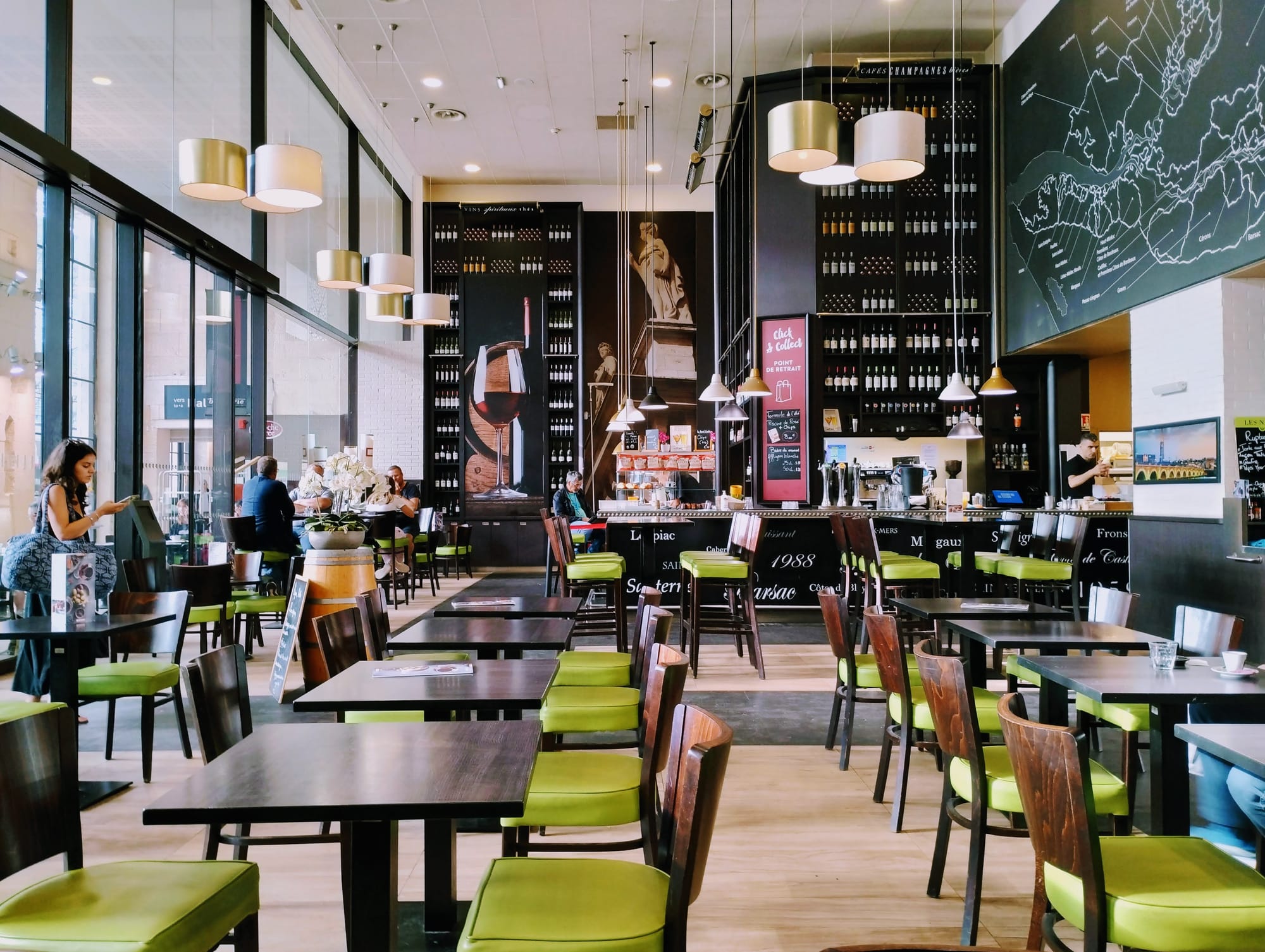 Wooden tables and green chairs lined up for service inside a bistro in the train station at Bordeaux.