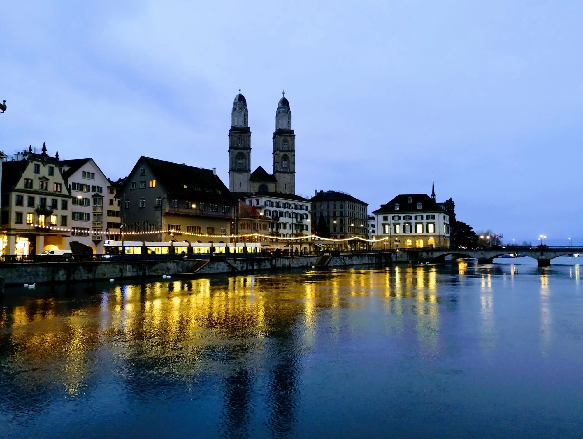 The two towers of the Grossmünster are reflected in the Limmat along with the Christmas decorations along the riverside.