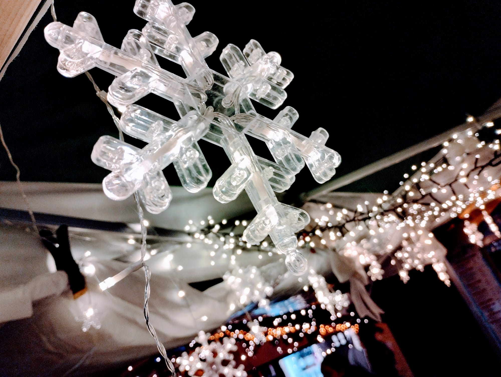 A white illuminated plastic snowflake against a background of white Christmas lights.