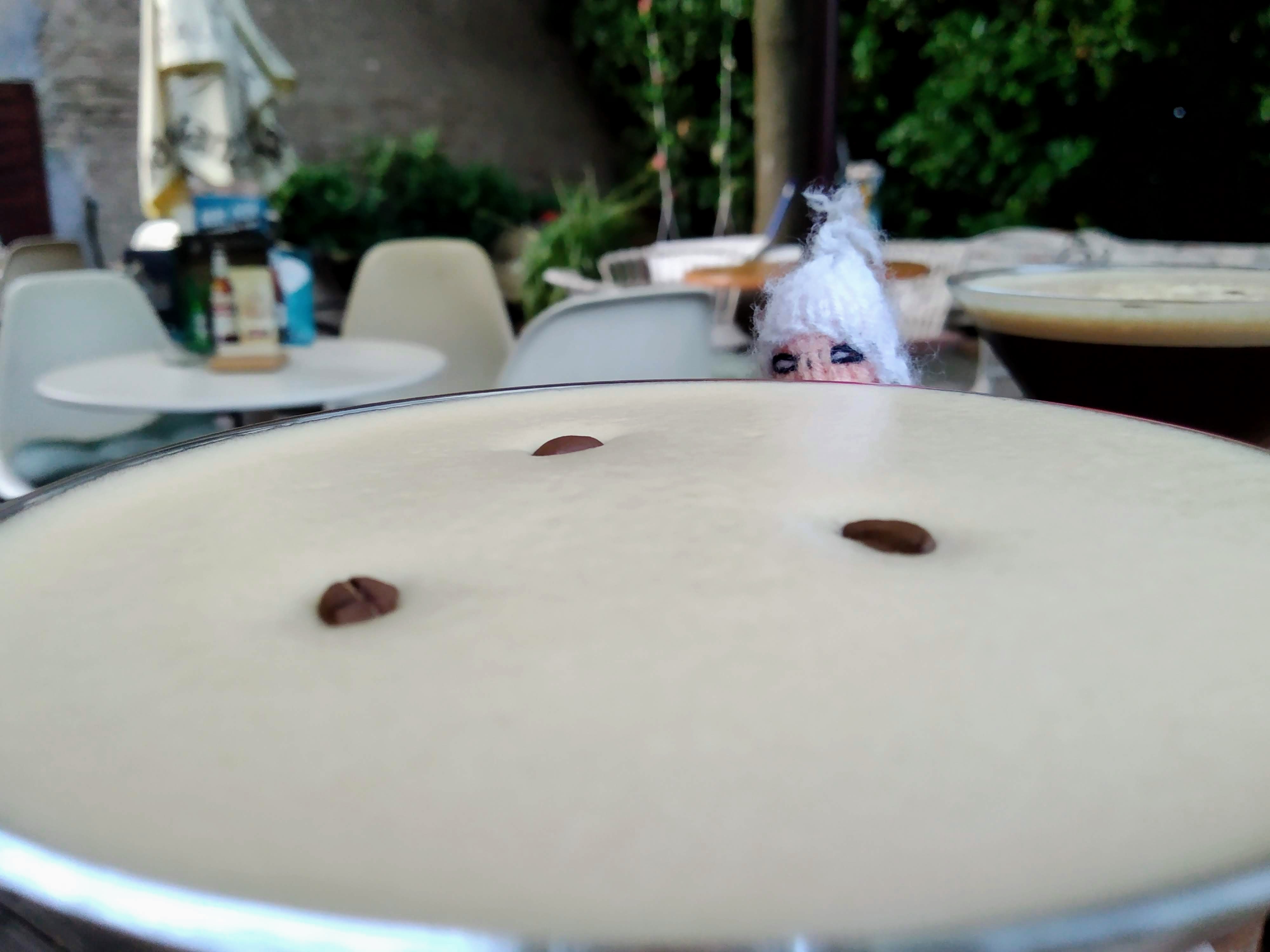 A puppet salivates from behind a close-up creamy, light brown cocktail in a martini glass, garnished with three coffee beans.