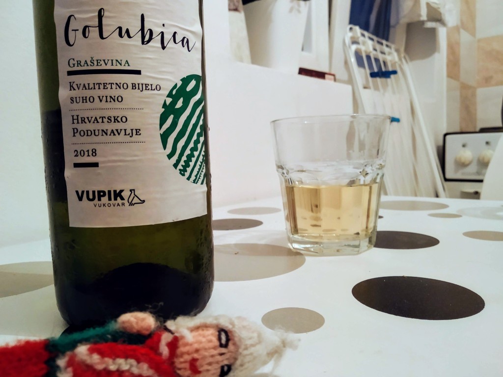 A hedonistic finger puppet sleeping off a bottle of Golubica Graševina white wine with a partially filled glass of wine in the background.