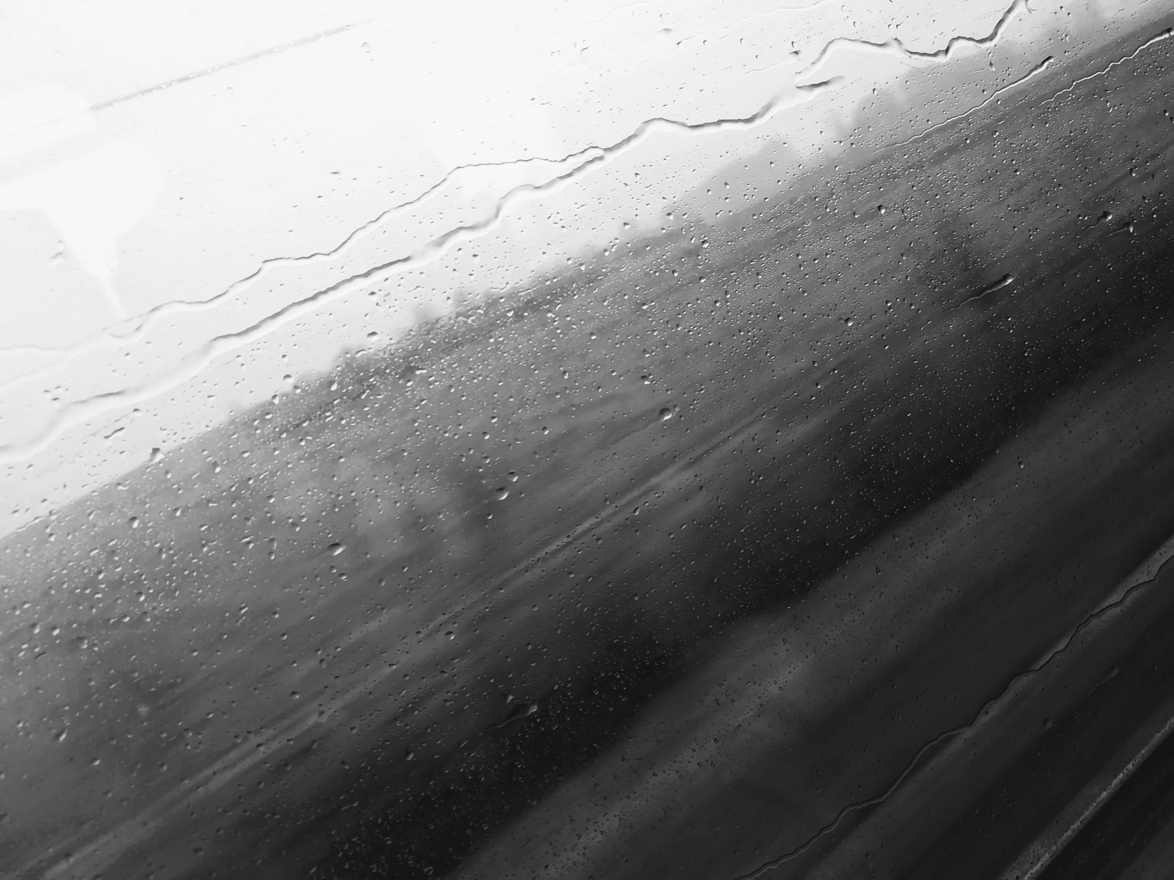 Raindrops and streaks on a window, with a gradient of light to dark grey, suggesting an outdoor scene.