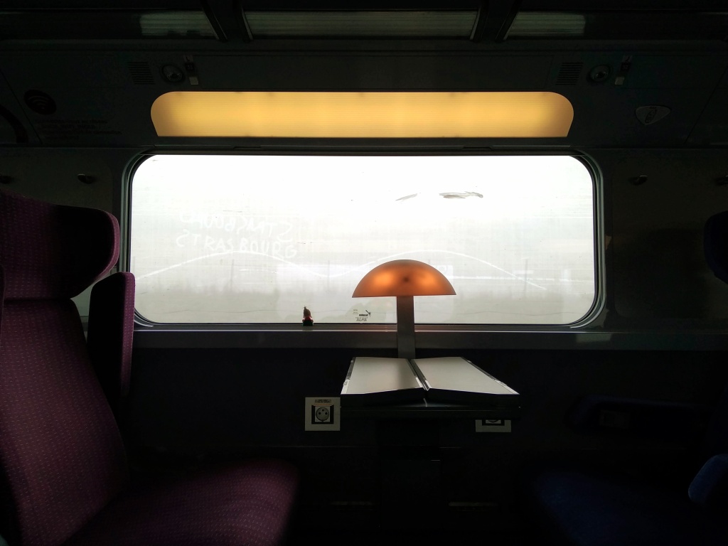 A finger puppet looks through a grimy window of a TGV.