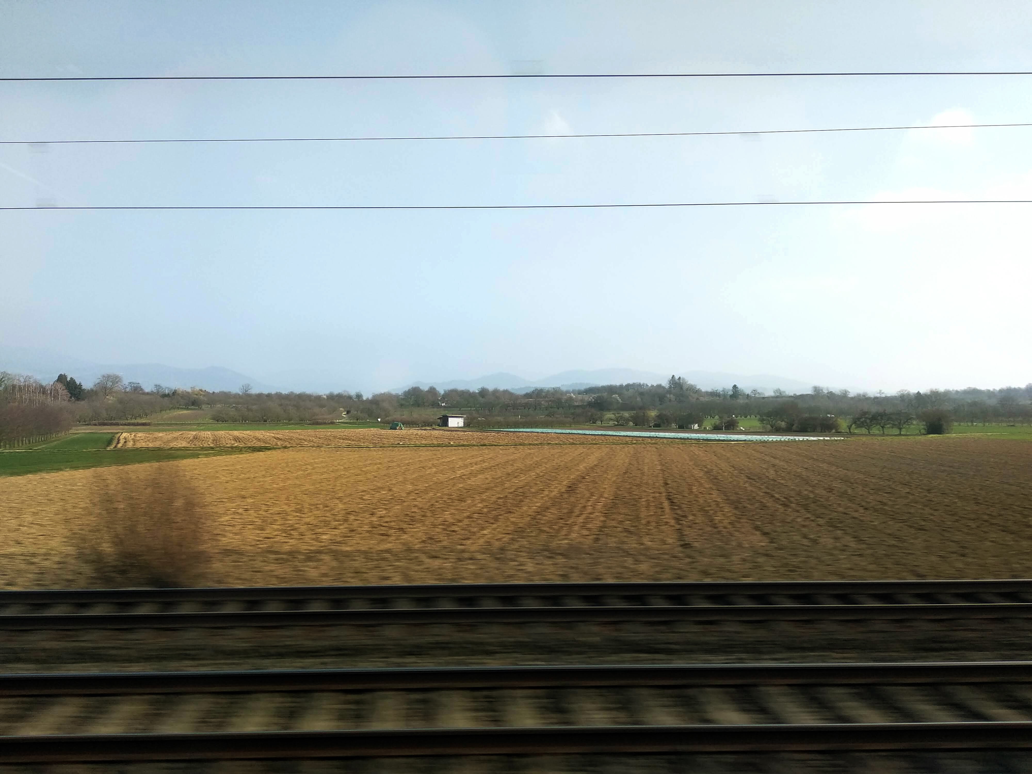 Ploughed farmland stretches to woodland on the horizon, mountains in the distance.