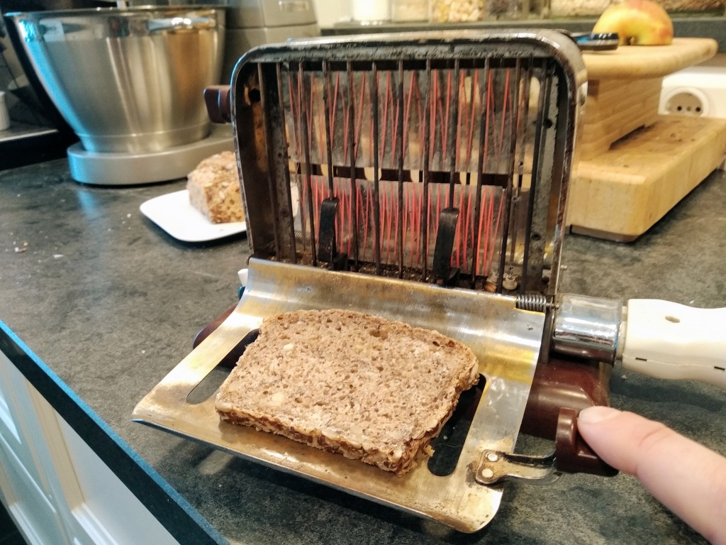 A slice of bread waiting to be toasted on an antique electric toaster.