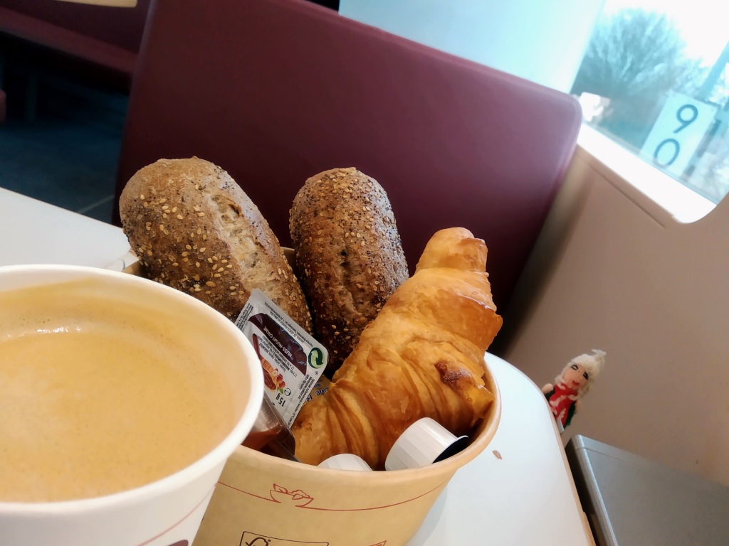 Two bread rolls, a croissant, assorted jam, and a mug of coffee.