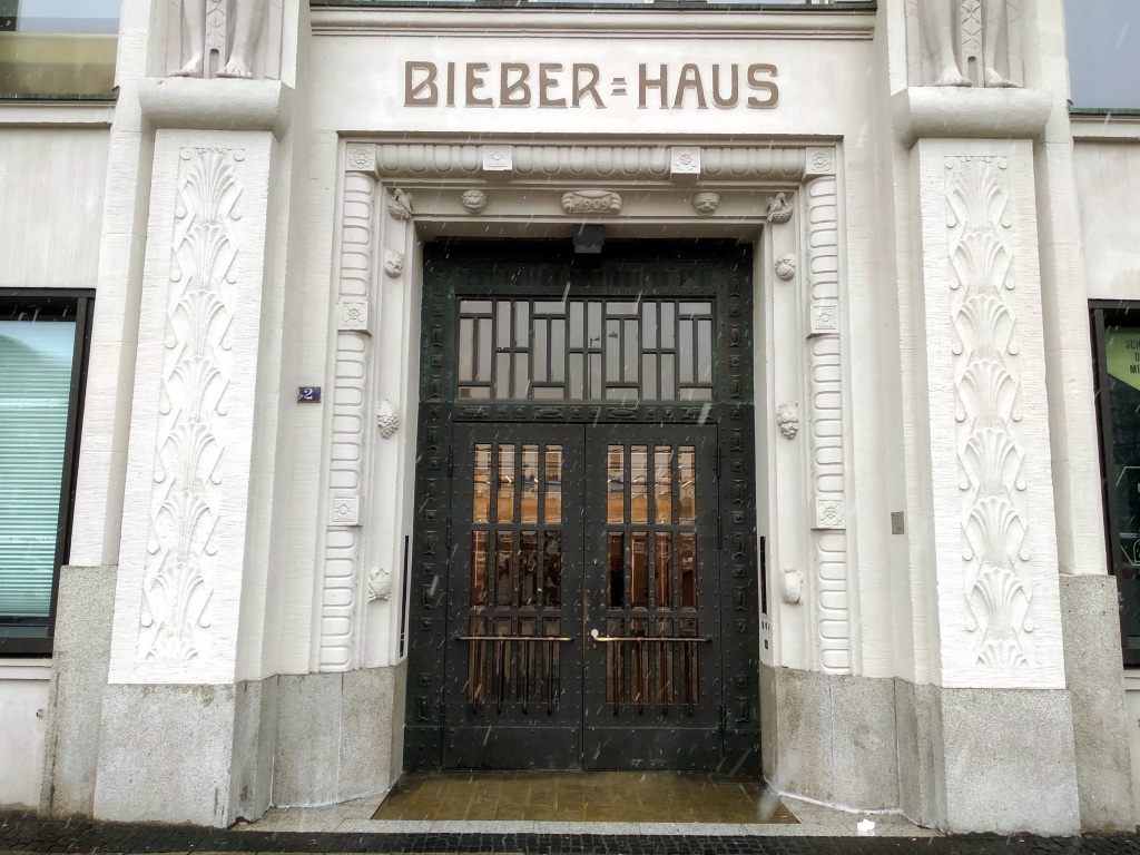 Iron doors with glass panels in an ornate white stone square arch under the words "Bieber Haus".