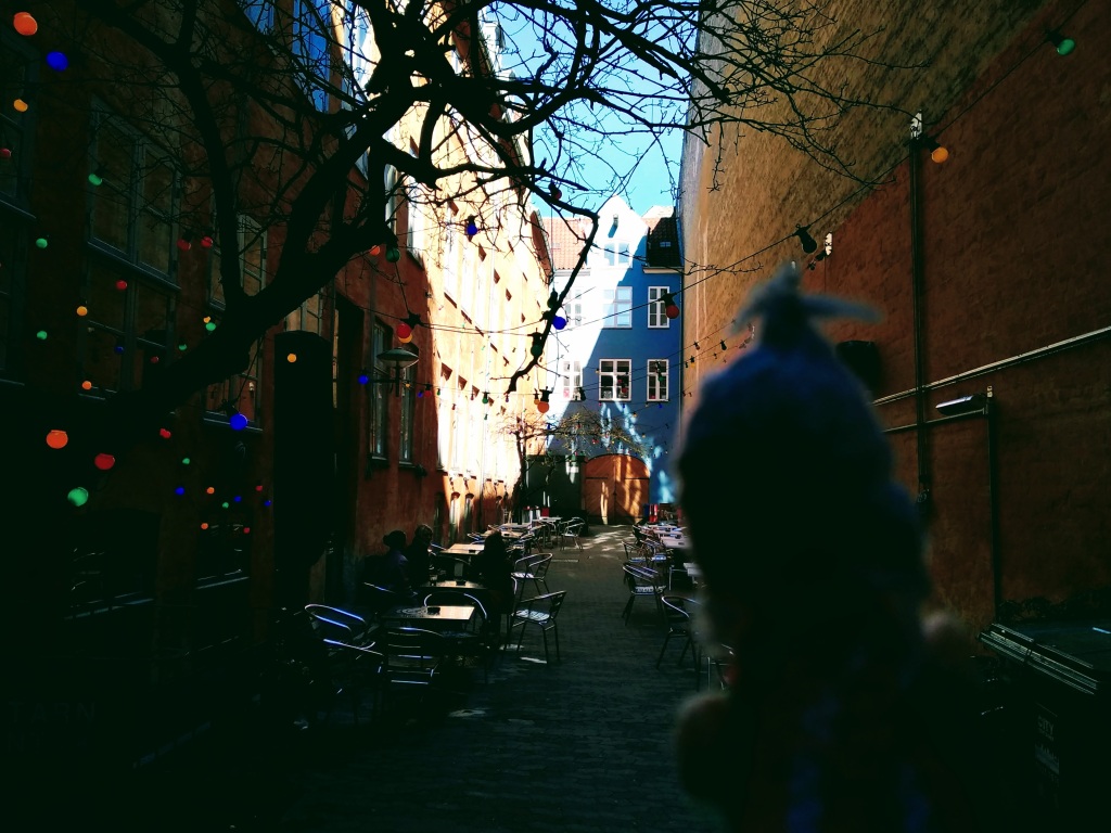 Coloured lights adorn the entrance to a shaded brick courtyard lined with silver tables and chairs.