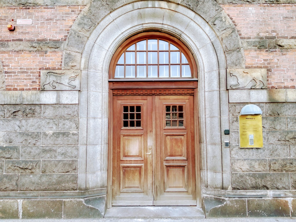 A faded brown wooden door in a stone arch in a stone and brick wall.