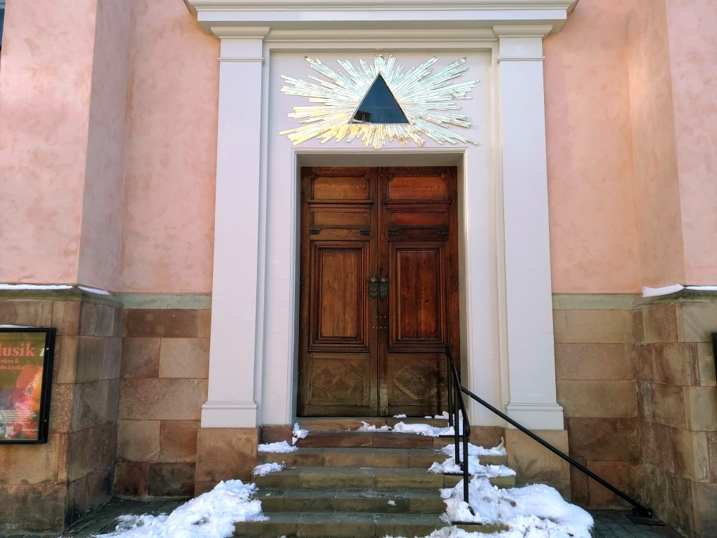 A large wooden door at the top of five snowy steps, set in a pastel pink wall.
