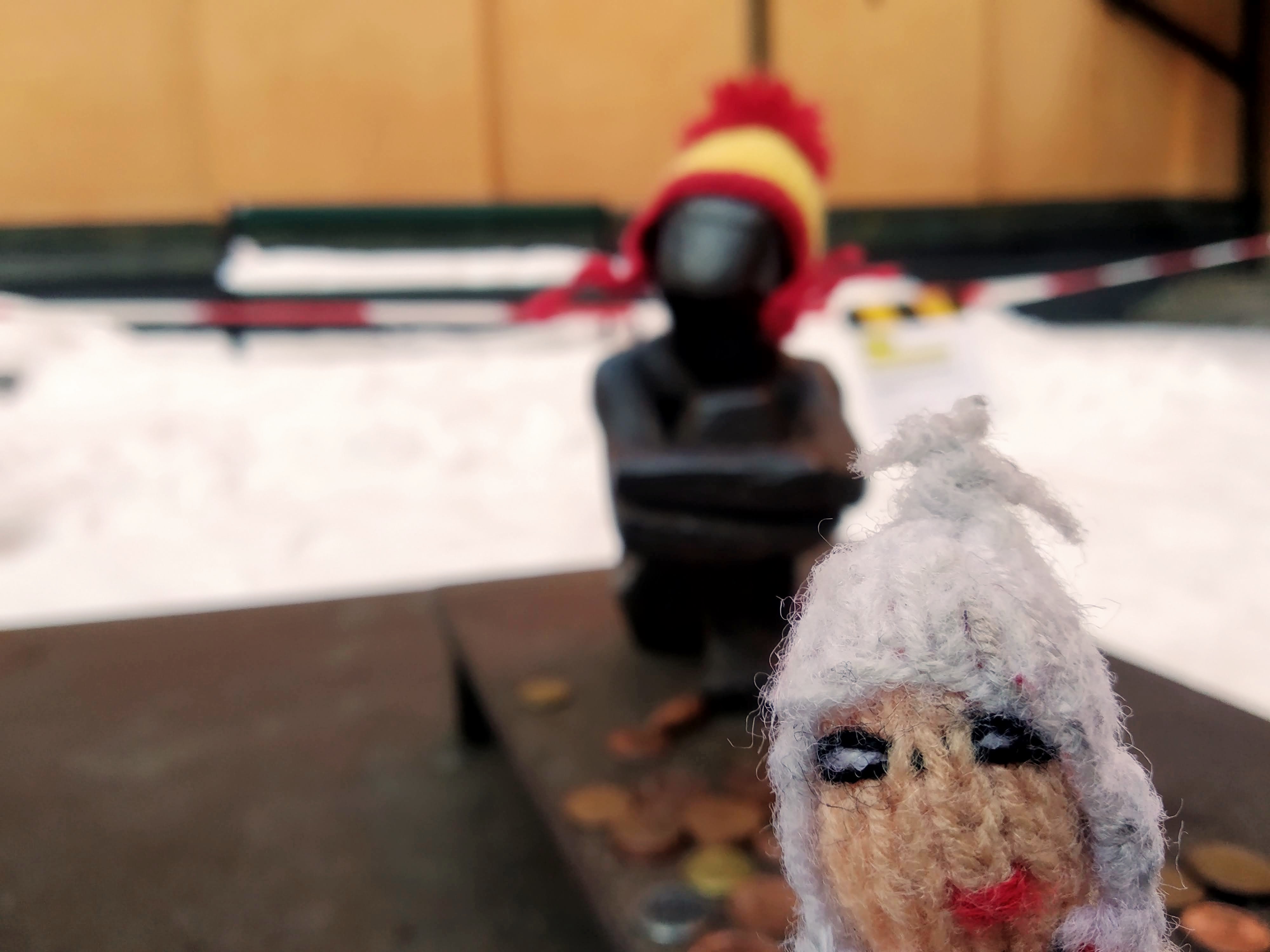 A small finger puppet in front of a small metal statue.