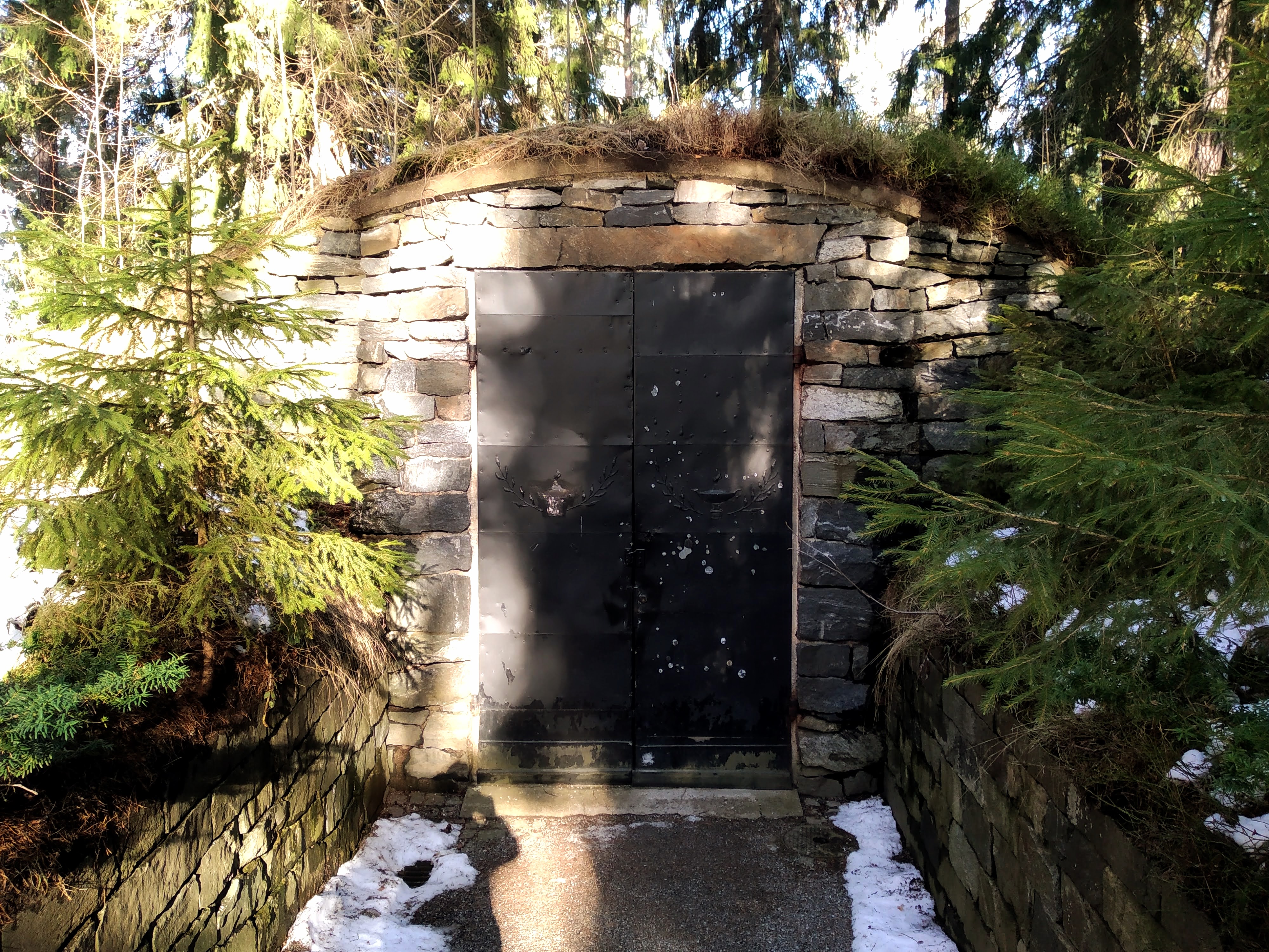 Metal door into a stone bunker surrounded by pine trees.