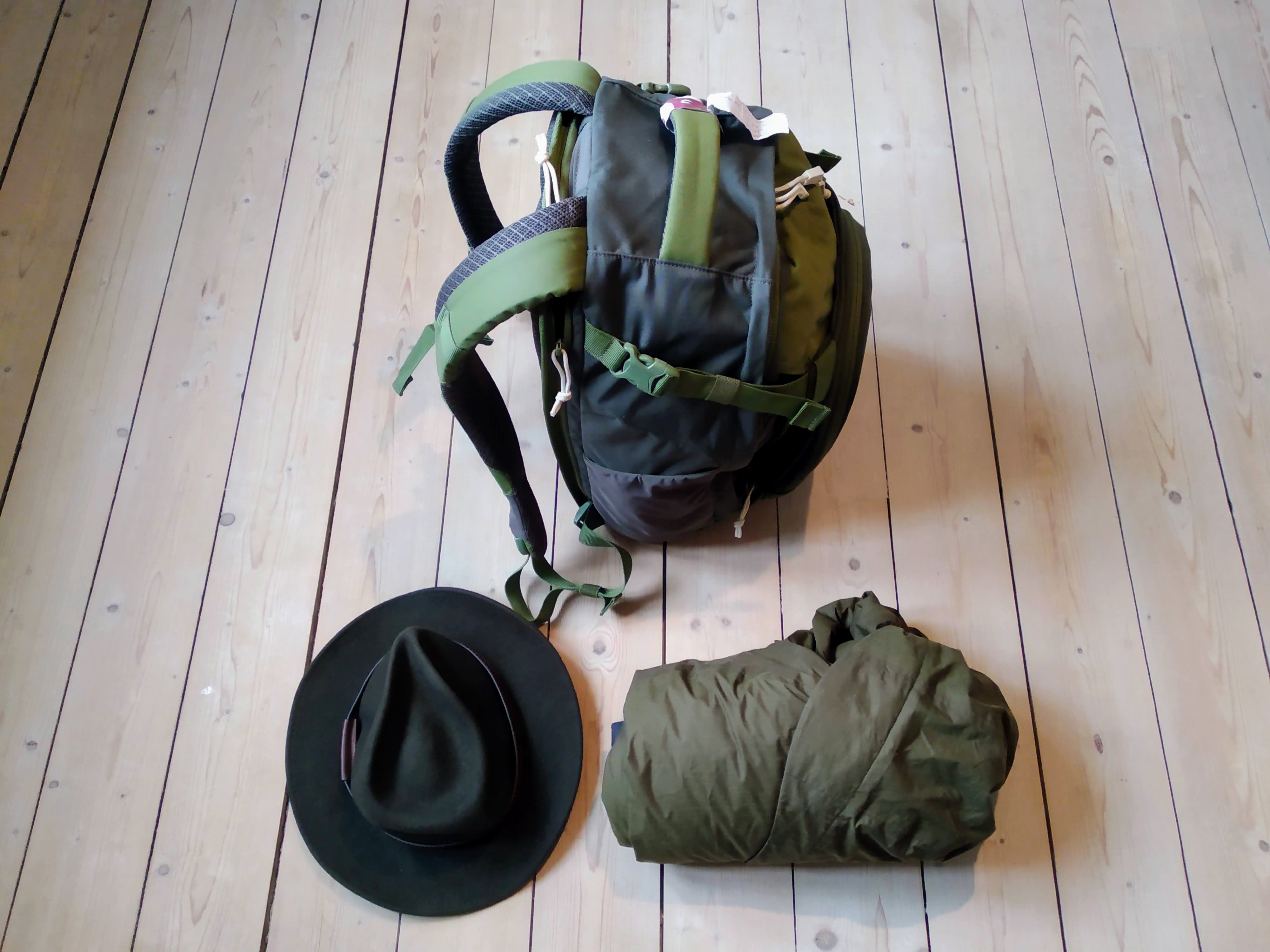 A felt hat and rolled-up waterproof next to a packed backpack.