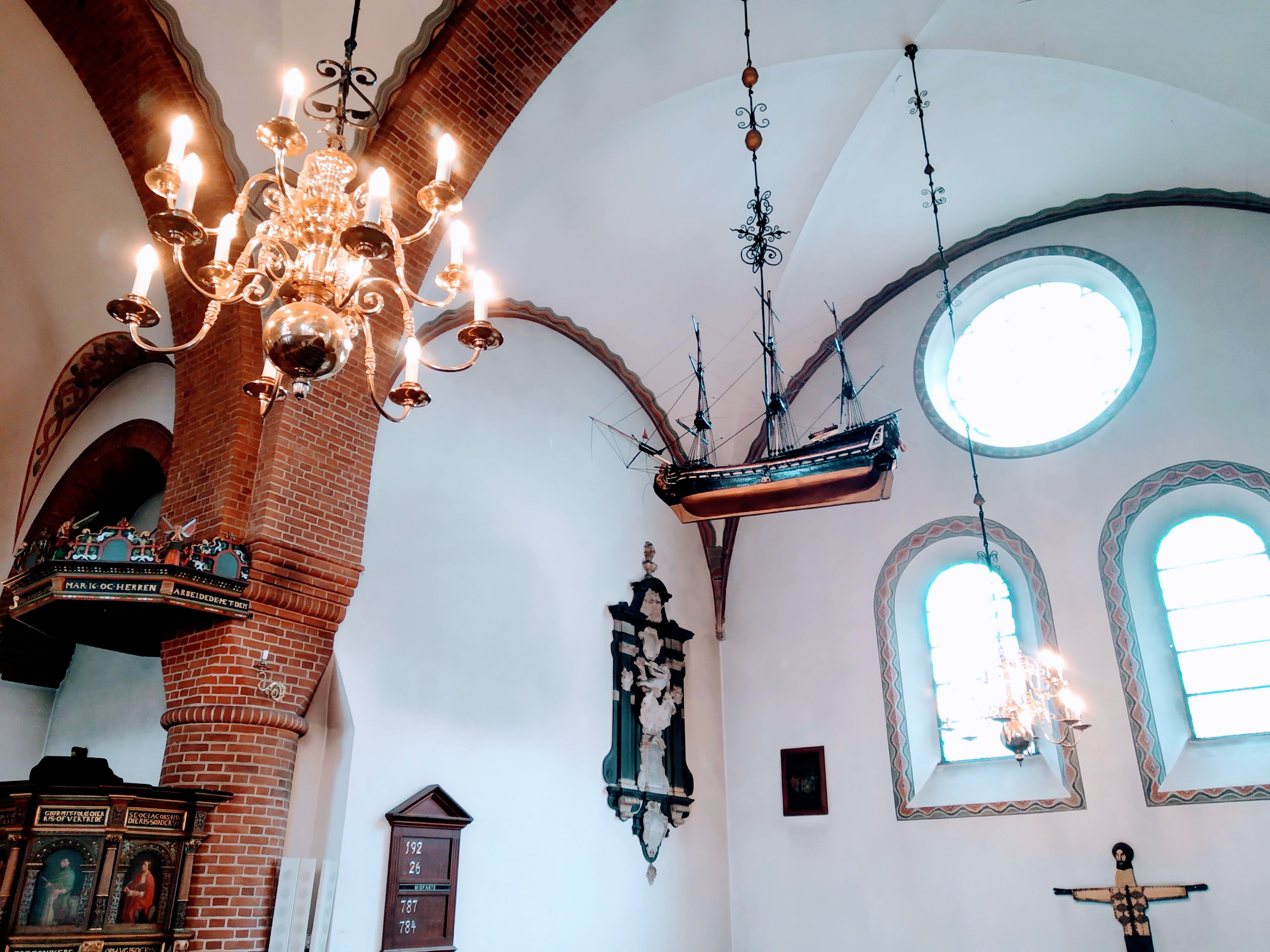 A model of a ship hanging alongside a chandelier from the vaulted ceiling of a church.