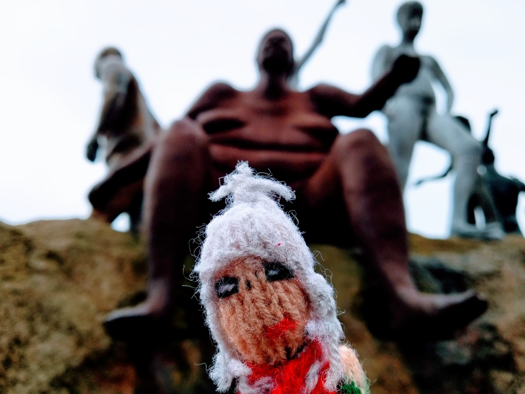 Finger puppet smiles between the loins of a large red metal lady.