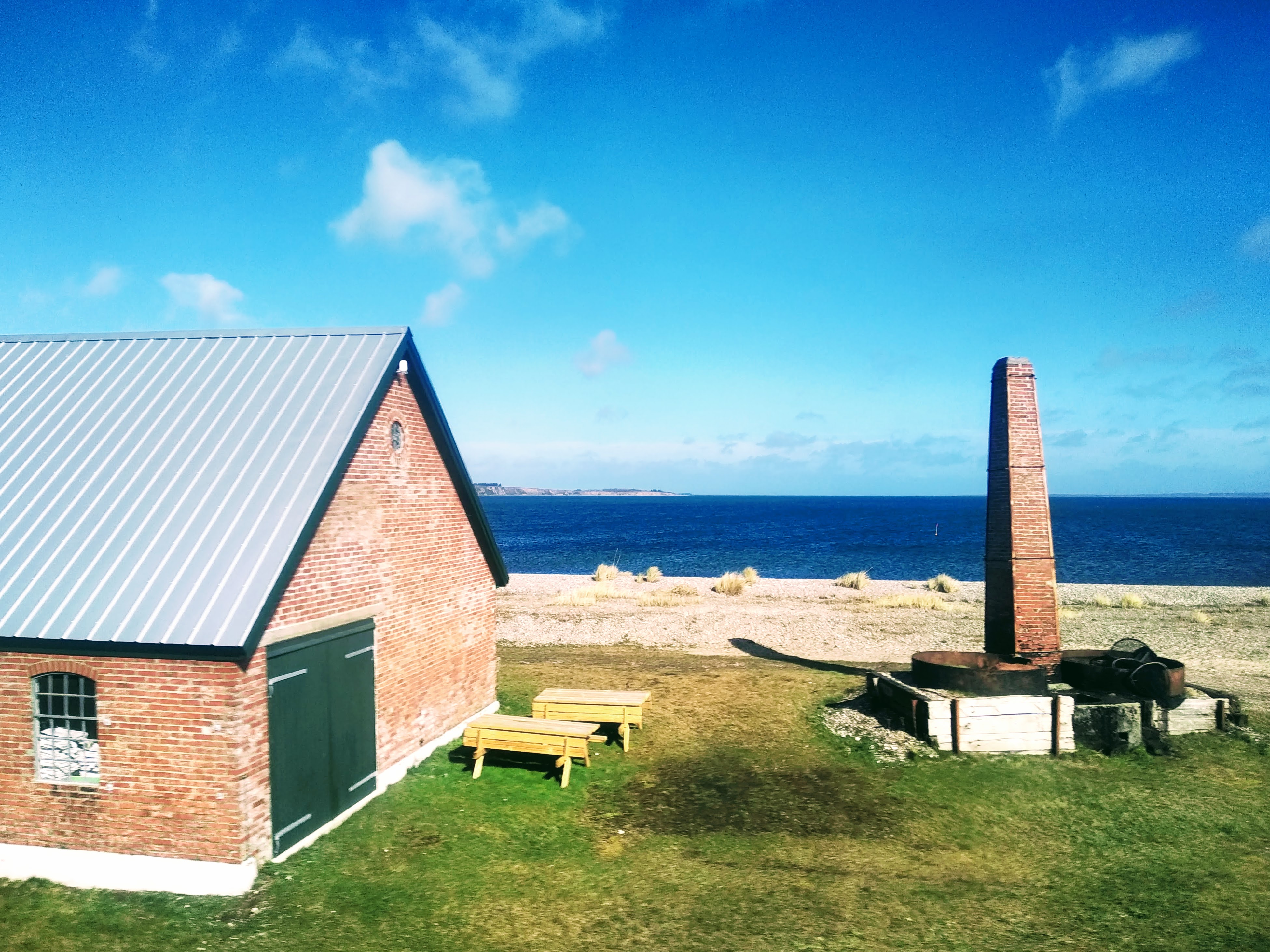 Green barn doors on the end of a red brick building on the shore of a fjord.