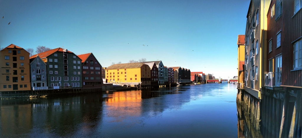 Colourful buildings line and are reflected in the Nidelva river.