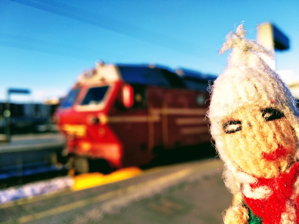 A red and yellow train with a snowplough is admired by a slightly frosty finger puppet.