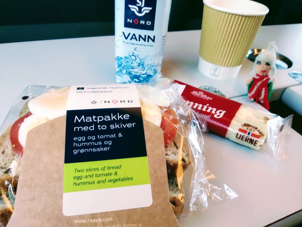 A complimentary breakfast of bread with egg and tomato and hummus and vegetables served with coffee and a Lefse.