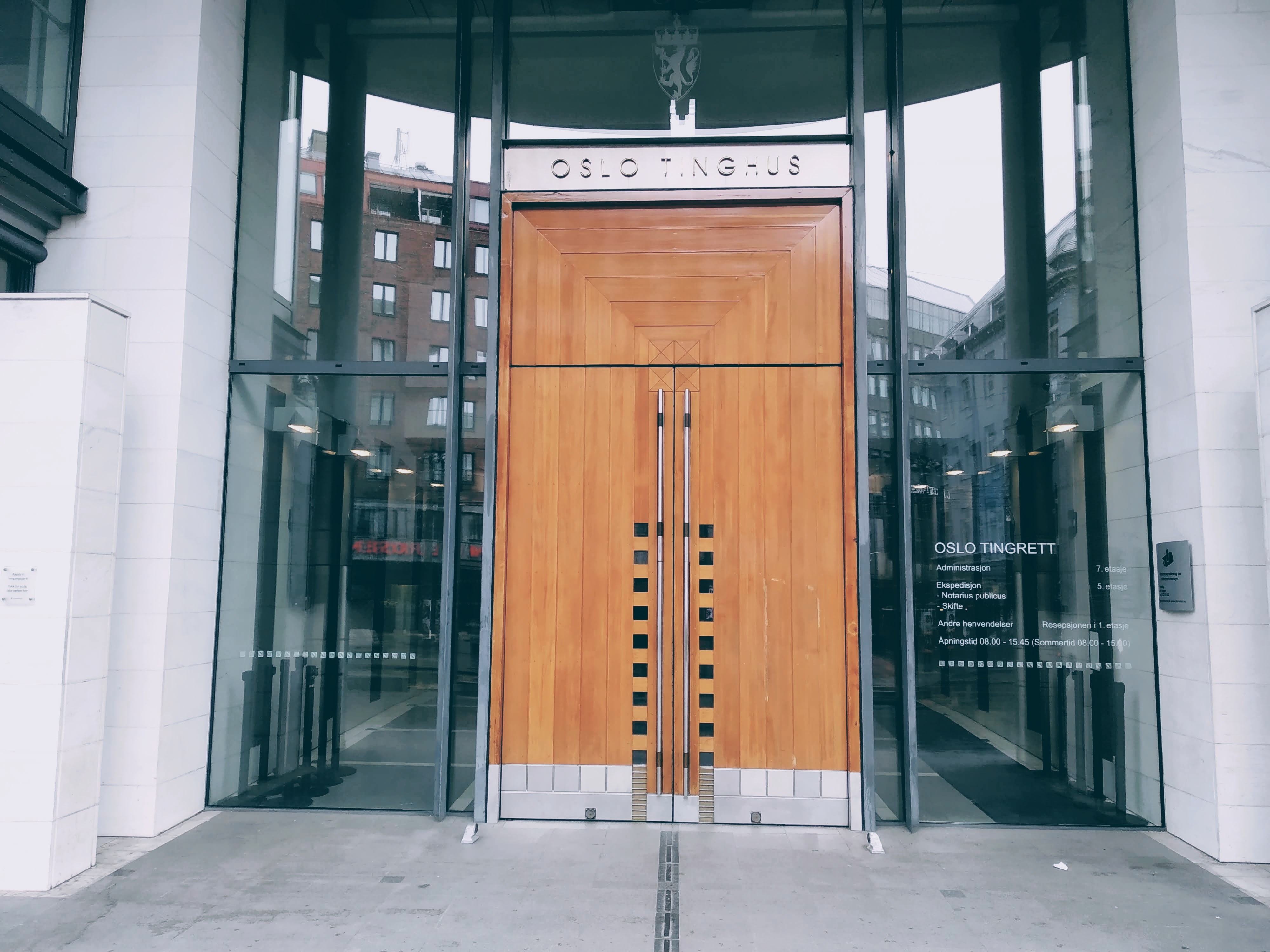 The grand wooden door of the Oslo Tinghus surrounded by plate glass windows.