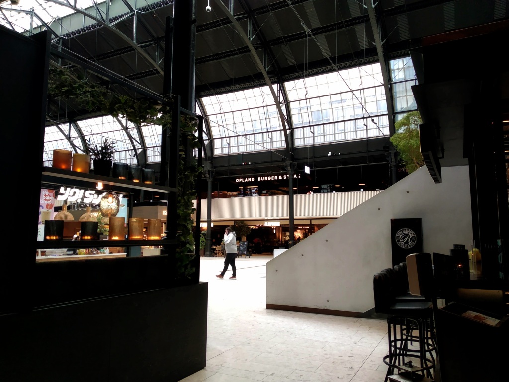 Among modern restaurants, a man speaks on the phone in the old train hall of Oslo Sentralstasjon.
