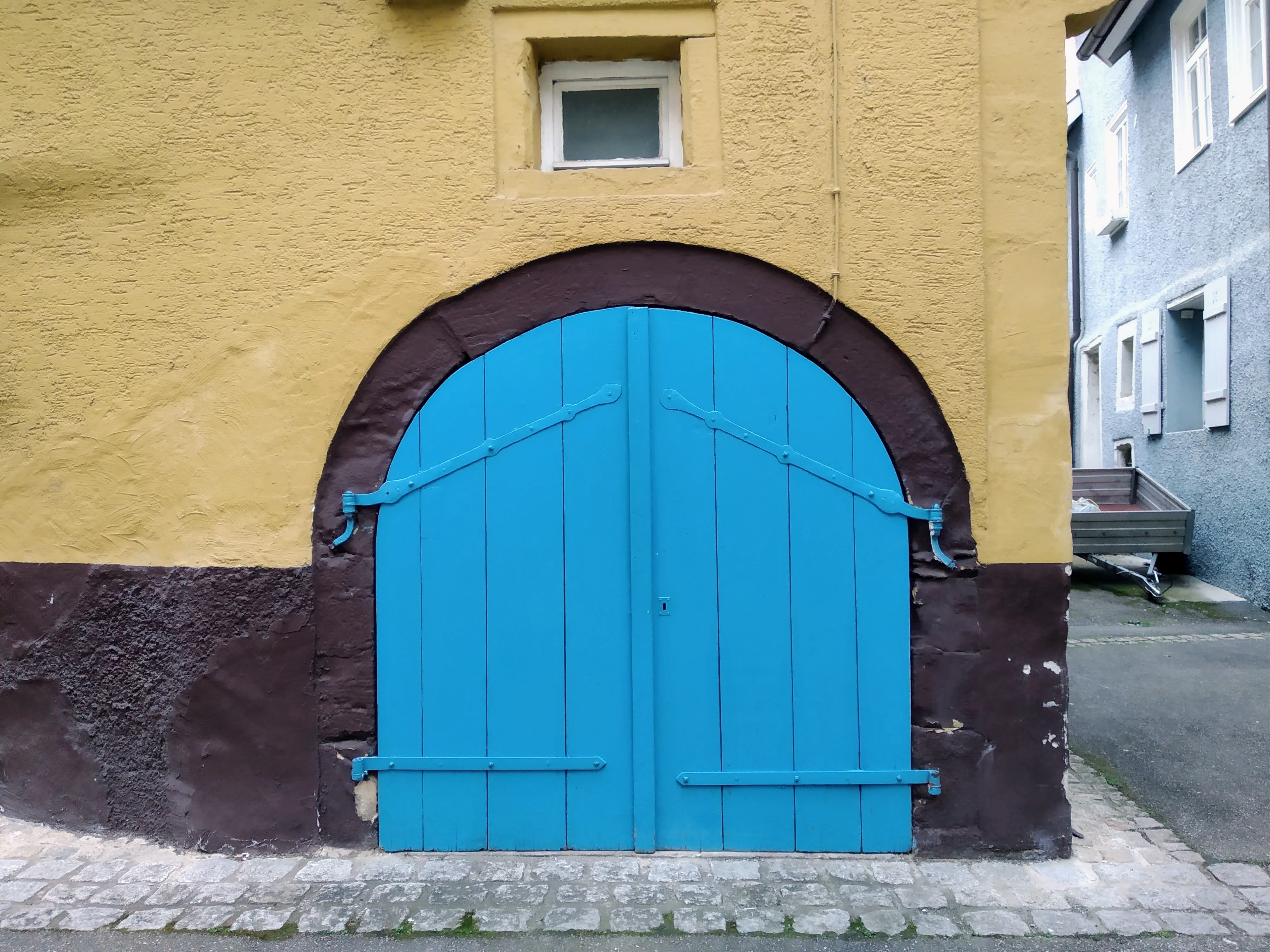 A painted arched blue wooden door in a brown and cream wall.