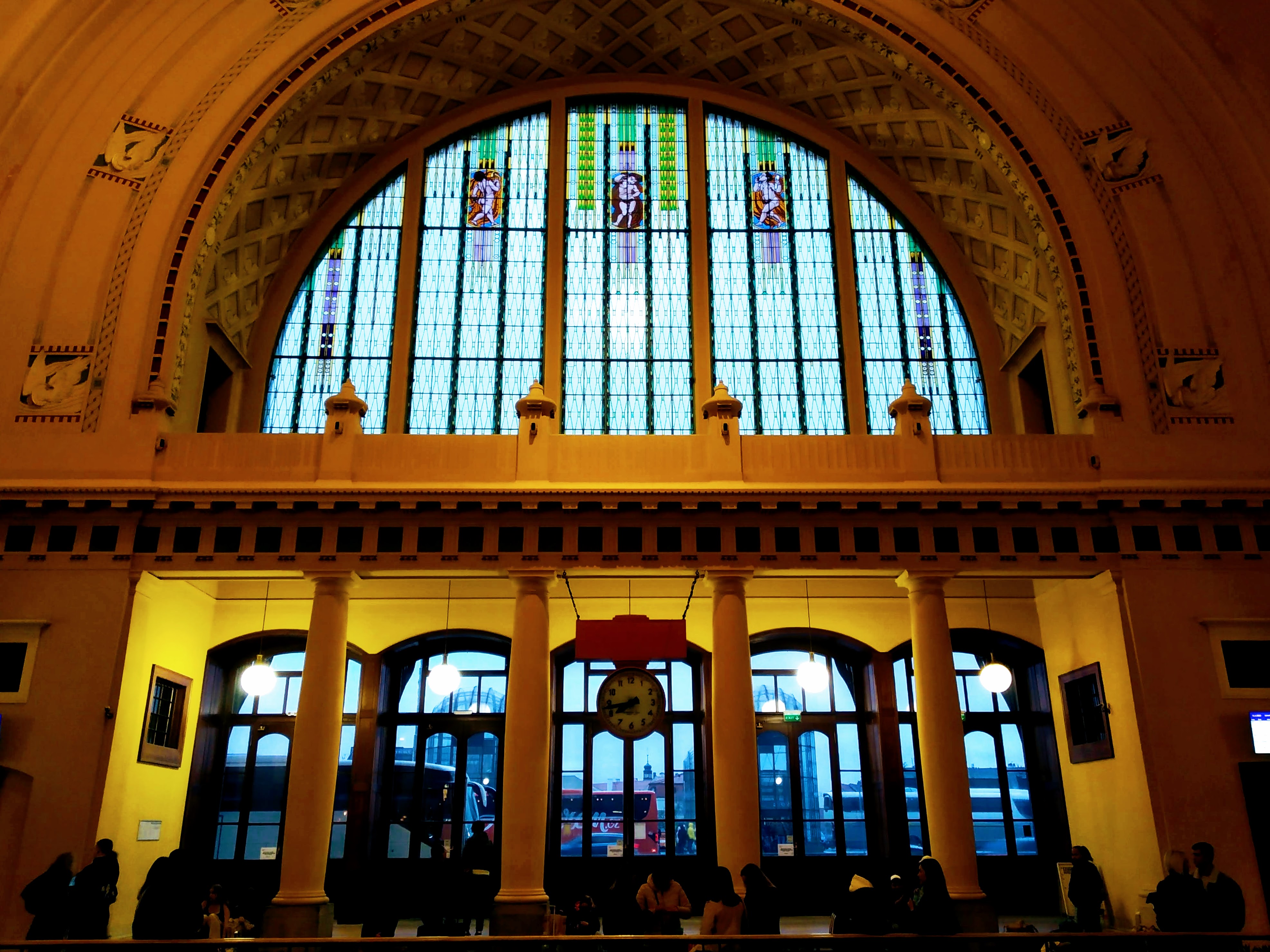 Doors of the old part of Praha Hlavní Nádraží under an arch of stained glass.