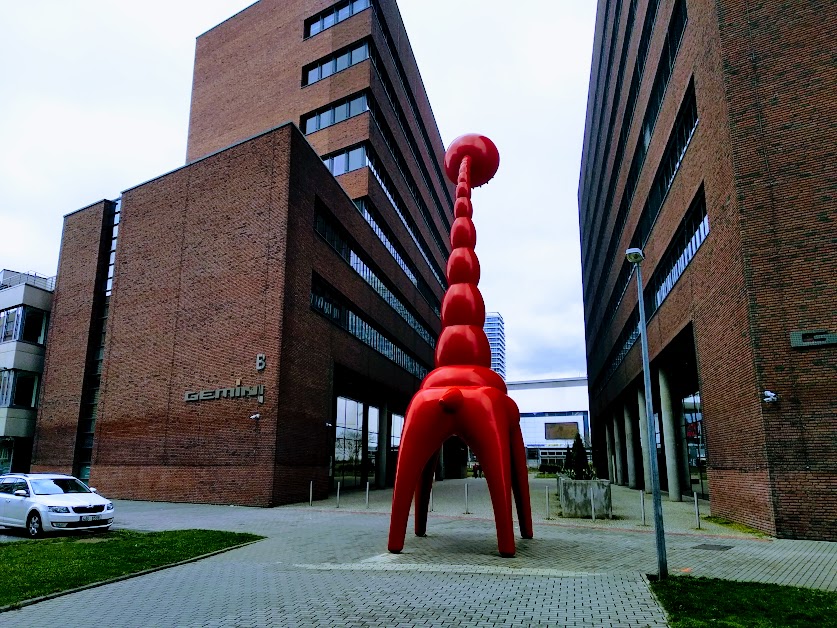 Photograph of the arse end of a massive red plastic giraffe with a shower-head for a face.
