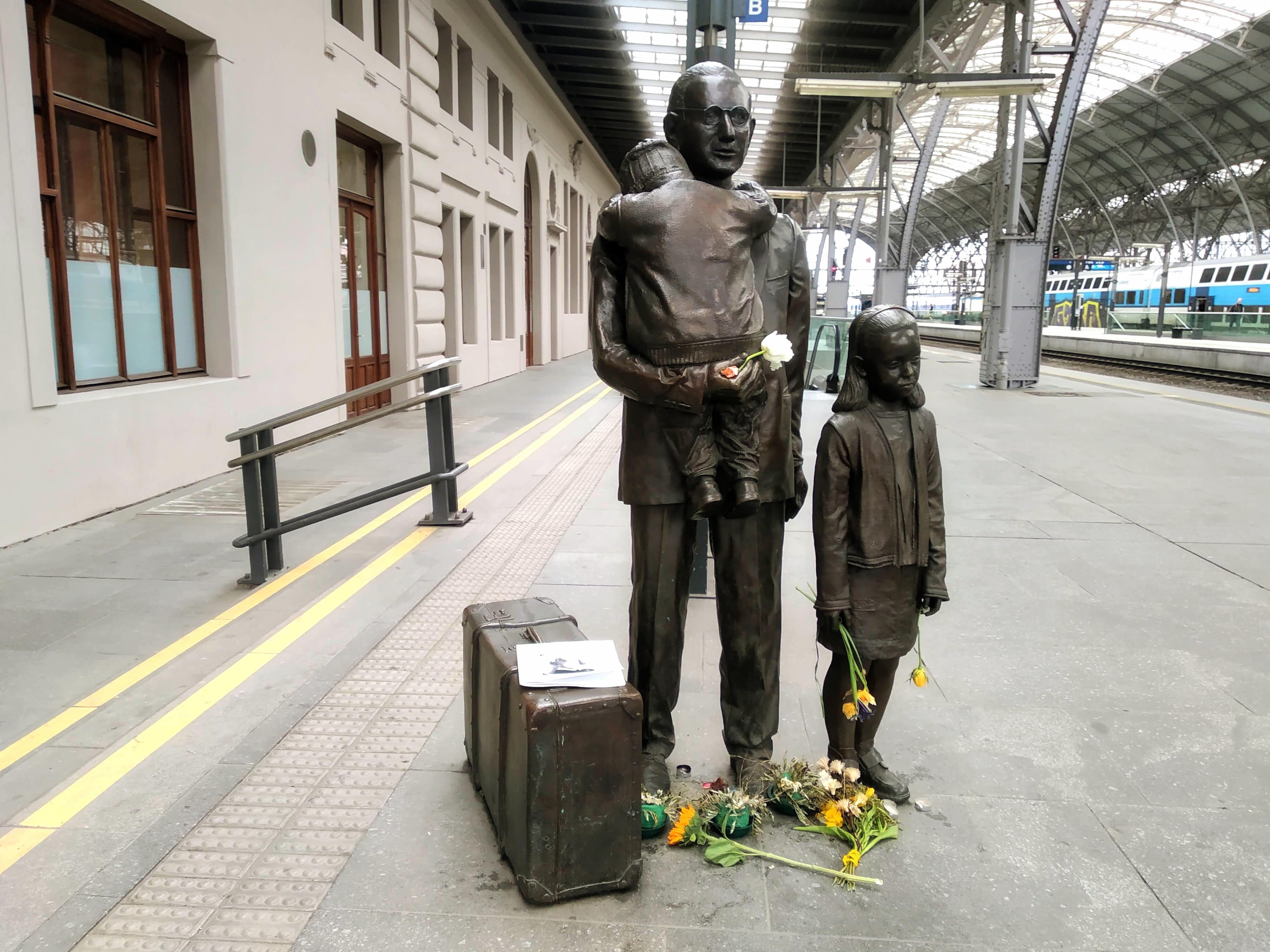 A statue commemorating Nicholas Winton in Prague Central Station, on which people have placed flowers.