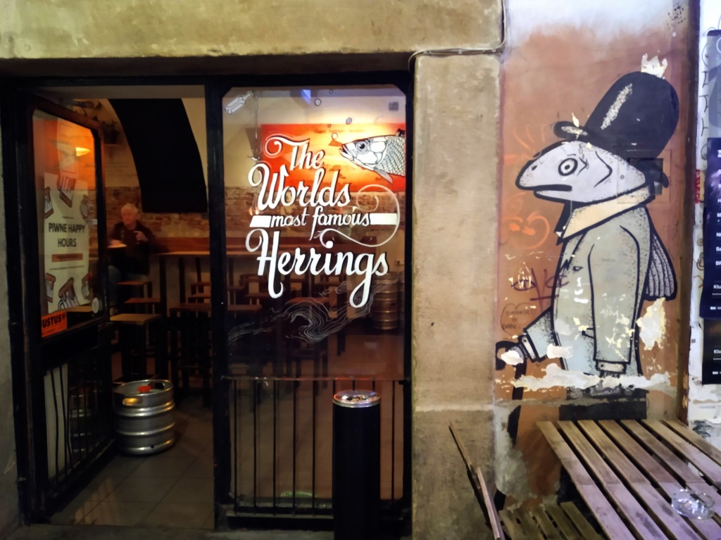 A picture of a glass door into a restaurant on which is written "The world's most famous herrings". There is a stylised illustration of a herring wearing a hat on the wall next to the door.