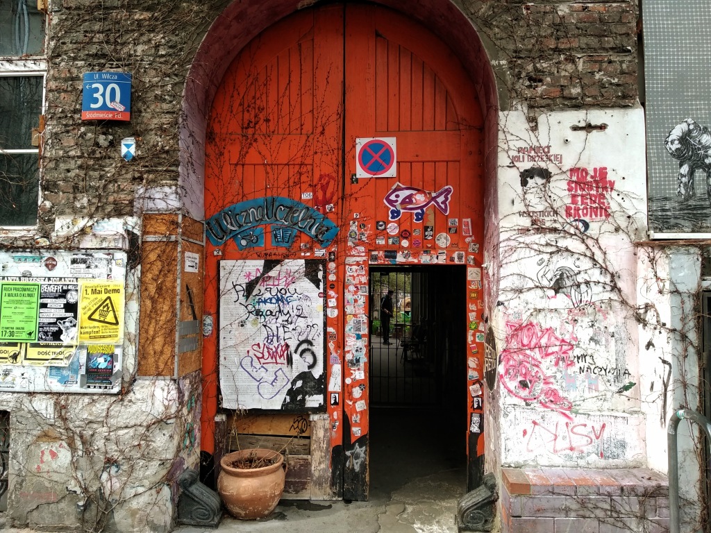 A large red wooden door in a brick arch leads to a gated courtyard.