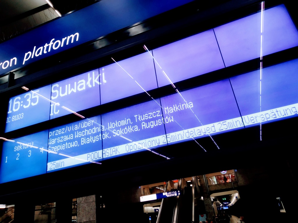 A platform information display showing a delayed train to Suwałki.